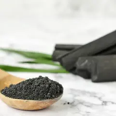 Drewniana łyżka z proszkiem, obok kawałki węgla aktywnego.