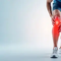 Mężczyzna trzyma się za nogę, odczuwając ostry ból pod kolanem. Czerwony obszar podkreśla miejsce urazu.