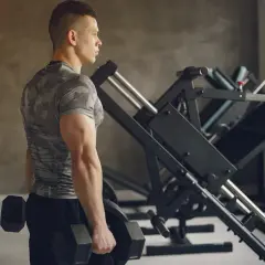 Mężczyzna z dobrze rozwiniętym tricepsem trzyma hantle w siłowni, gotowy do treningu.