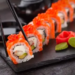 Chopsticks podnoszą kawałek sushi z łososiem i ikrą. Czy sushi jest zdrowe? Tak, jeśli jest przygotowane z ryżem, rybą i warzywami.