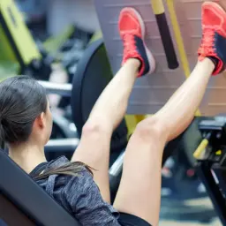 Kobieta ćwiczy na maszynie leg press, wykonując ćwiczenie na nogi.