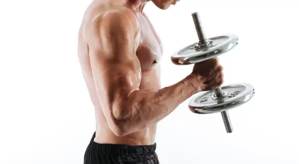 Mężczyzna ćwiczy biceps z hantlem. Widać napięte mięśnie i pot na skórze.