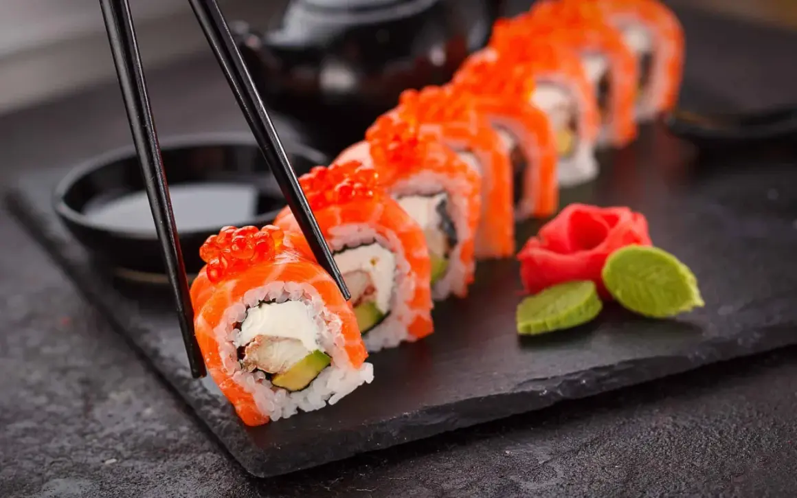 Chopsticks podnoszą kawałek sushi z łososiem i ikrą. Czy sushi jest zdrowe? Tak, jeśli jest przygotowane z ryżem, rybą i warzywami.