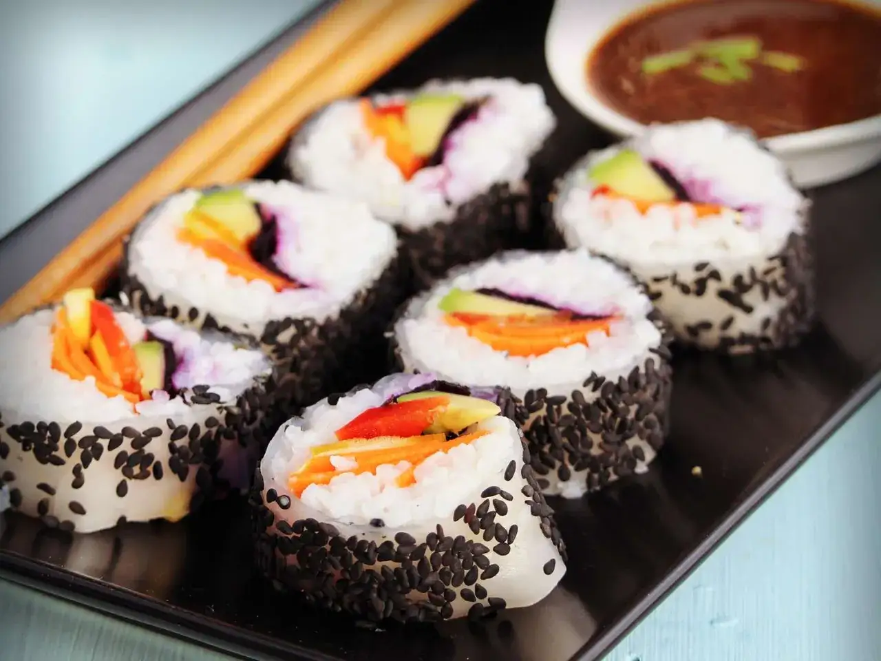 Siedem kawałków sushi z czarnym sezamem, awokado i marchewką. Czy sushi jest zdrowe? Tak, jeśli jest przygotowane z dobrych składników.