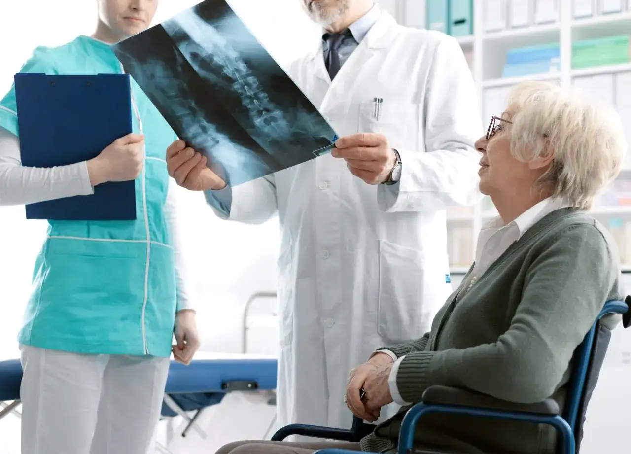 Lekarz omawia z pacjentką na wózku inwalidzkim wyniki prześwietlenia kręgosłupa, wskazując na możliwe objawy osteoporozy.
