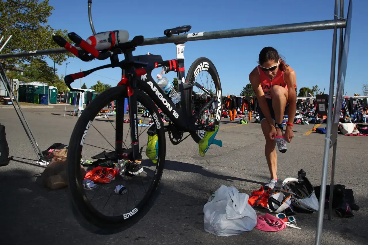 Kobieta zakłada skarpetki przy rowerze triathlonowym, gotowa na długi dystans iron man.