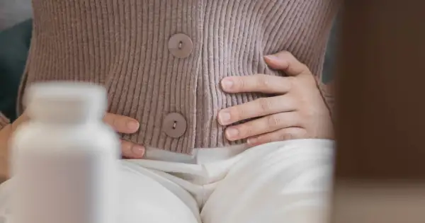 Kobieta trzyma się za brzuch, szukając ulgi na wzdęcia. Obok stoi biała butelka z lekami.