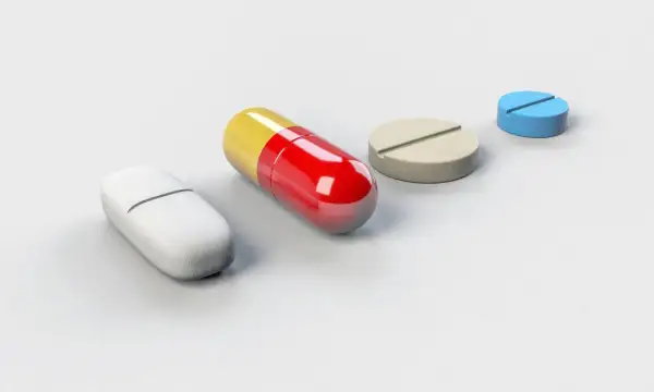 Różne tabletki i kapsułka, być może zawierające tryptofan, na białym tle.